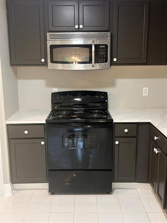 21216 Gardenia St, Covington, LA 70435 - kitchen with stainless steel microwave, black electric range oven, light tile patterned floors, and light stone counters