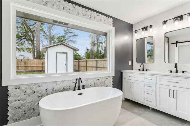 bathroom featuring double vanity, a healthy amount of sunlight, a freestanding bath, and a sink