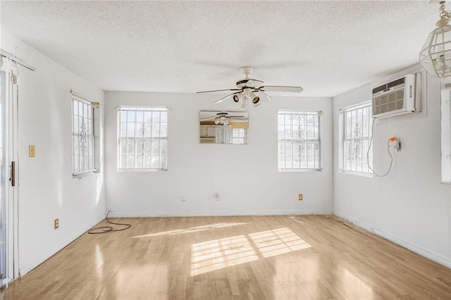 interior space with a wall mounted air conditioner, a textured ceiling, baseboards, a ceiling fan, and light wood-style floors