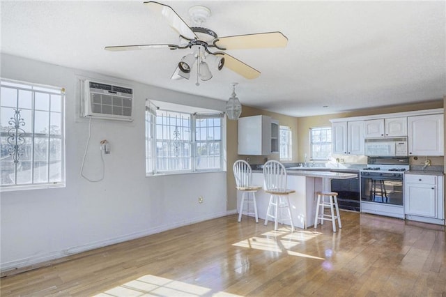 kitchen featuring white appliances, a kitchen bar, a ceiling fan, light wood-type flooring, and a wall unit AC