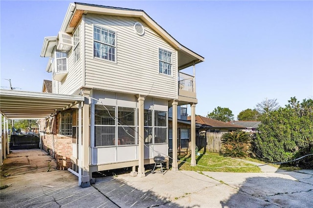 back of house featuring a balcony, driveway, a carport, and fence