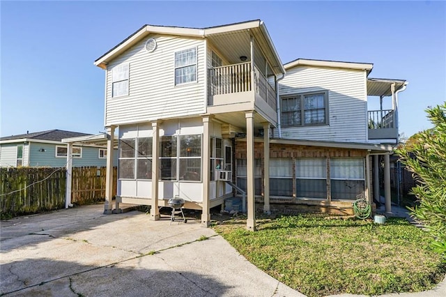 rear view of property with a balcony, a sunroom, and fence