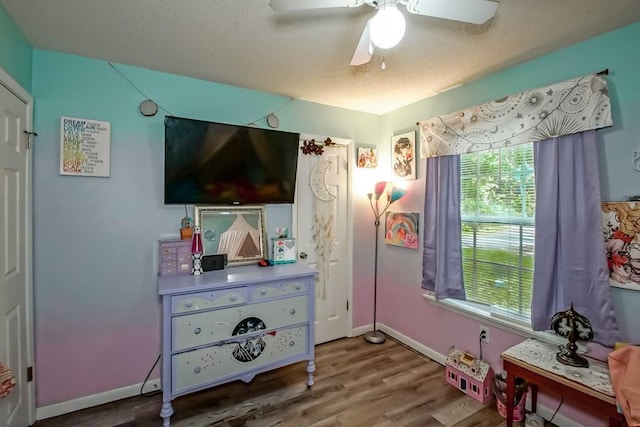 bedroom featuring ceiling fan, baseboards, multiple windows, and wood finished floors