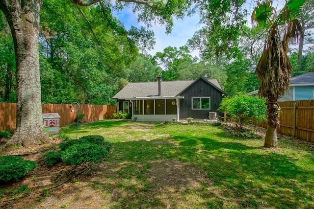 back of house featuring roof with shingles, a sunroom, a fenced backyard, a chimney, and a lawn