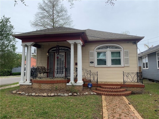 view of front of house featuring a front yard, a shingled roof, and a porch