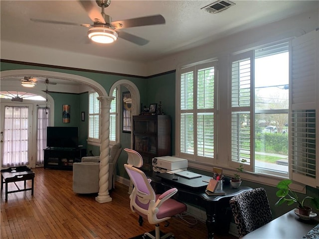 office area with decorative columns, arched walkways, hardwood / wood-style flooring, visible vents, and ceiling fan