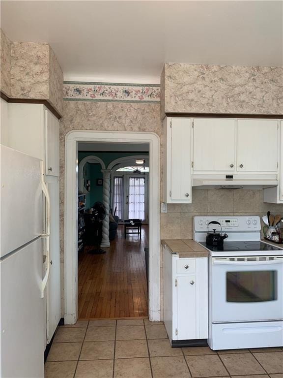 kitchen featuring tile counters, white appliances, under cabinet range hood, white cabinetry, and light tile patterned floors