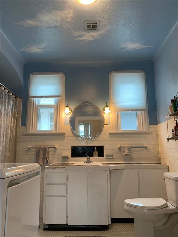 full bathroom featuring toilet, vanity, a textured ceiling, visible vents, and tile walls
