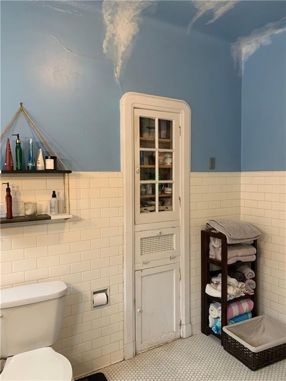 bathroom featuring a wainscoted wall, toilet, and tile walls