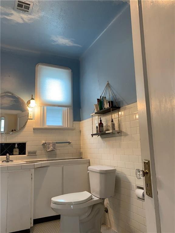 bathroom featuring tile walls, visible vents, toilet, and vanity