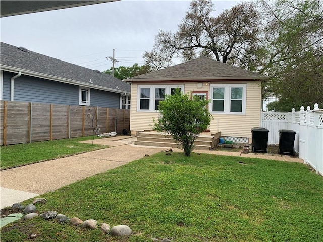 back of property featuring a fenced backyard, a shingled roof, and a yard