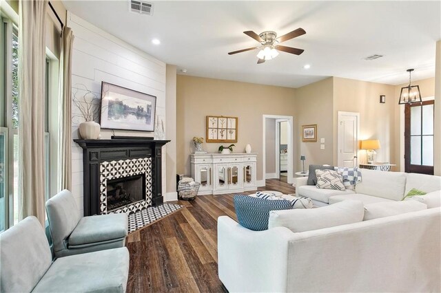 living area with ceiling fan with notable chandelier, visible vents, wood finished floors, and a tile fireplace