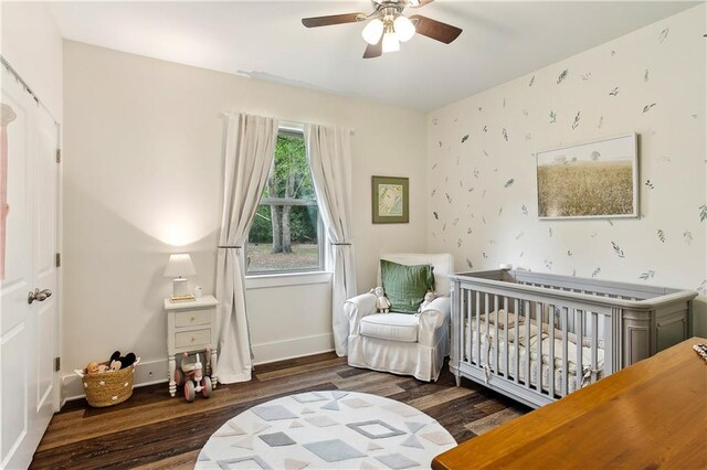 bedroom with baseboards, wood finished floors, a nursery area, and wallpapered walls