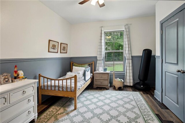 bedroom featuring a ceiling fan, wood finished floors, and wainscoting