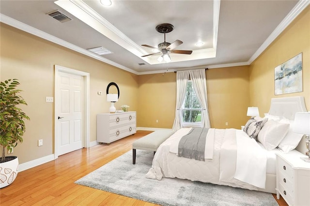 bedroom with baseboards, crown molding, visible vents, a raised ceiling, and light wood finished floors