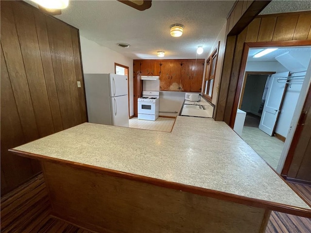 65 Willow Dr, Gretna, LA 70053 - kitchen with light countertops, a peninsula, white appliances, brown cabinets, and under cabinet range hood