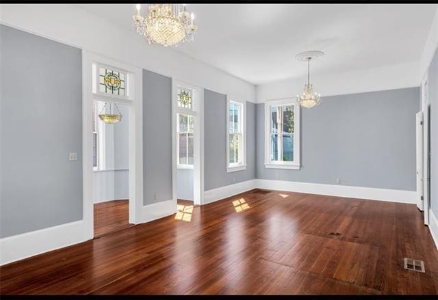 unfurnished dining area featuring baseboards, visible vents, wood finished floors, and an inviting chandelier