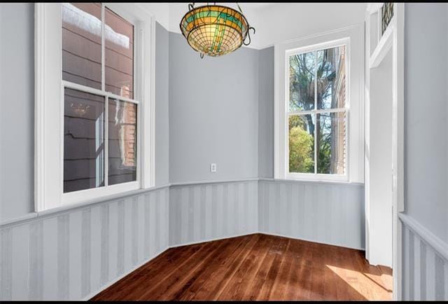 unfurnished dining area featuring dark wood finished floors and wainscoting