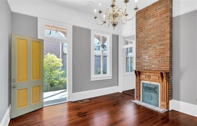 foyer entrance featuring an inviting chandelier, a brick fireplace, visible vents, and wood finished floors