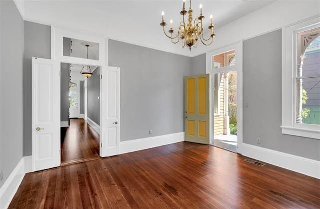 empty room featuring baseboards, visible vents, a chandelier, and wood finished floors