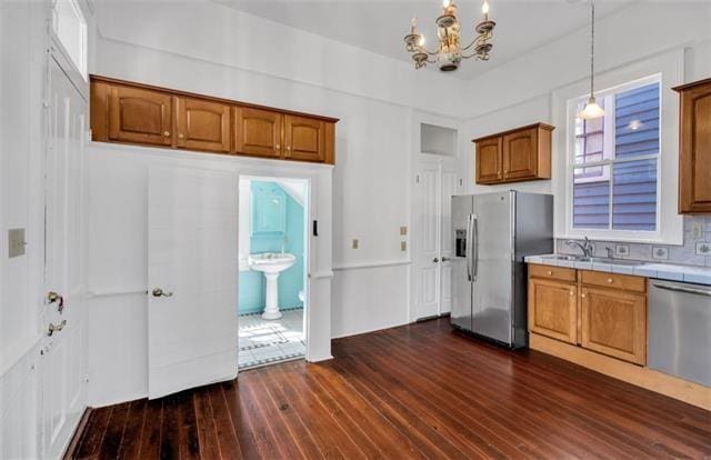kitchen with dark wood-style flooring, brown cabinets, appliances with stainless steel finishes, tile countertops, and a sink