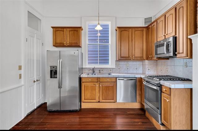 kitchen featuring a sink, tasteful backsplash, dark wood finished floors, stainless steel appliances, and tile countertops