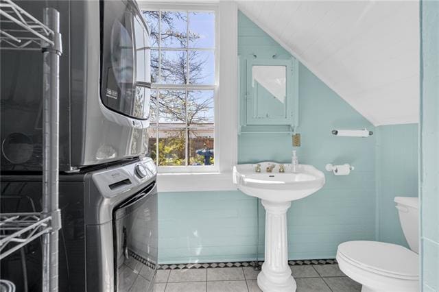 half bathroom featuring stacked washer / dryer, toilet, tile patterned flooring, and vaulted ceiling