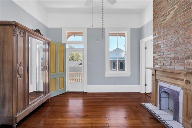interior space with baseboards, a fireplace with raised hearth, a ceiling fan, brick wall, and wood-type flooring