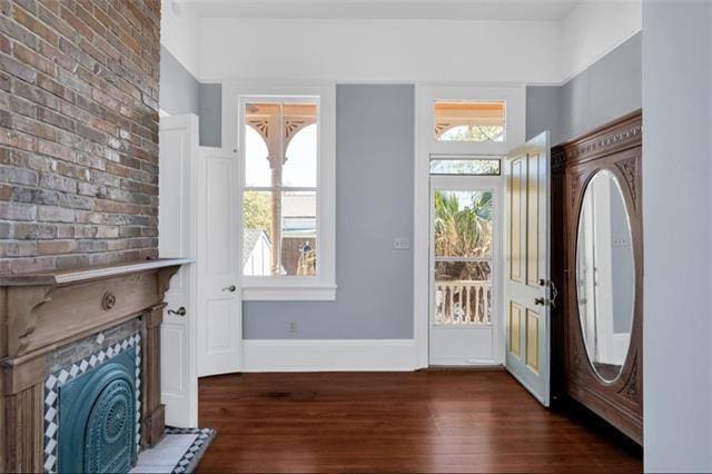 foyer entrance featuring baseboards, dark wood-style flooring, a fireplace, and brick wall