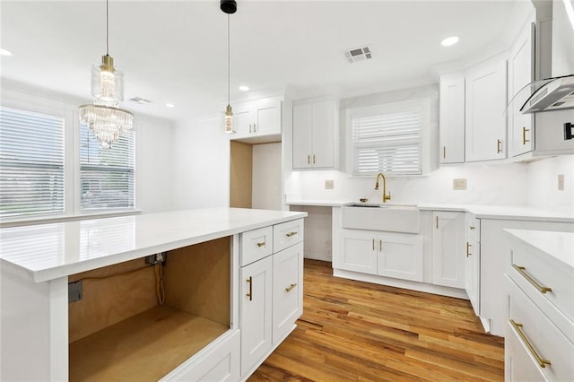 3839 Johnson St, Metairie, LA 70001 - kitchen featuring a sink, wall chimney range hood, light wood-type flooring, hanging light fixtures, and white cabinetry