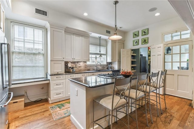 4209 Vendome Pl, New Orleans, LA 70125 - kitchen featuring a breakfast bar area, a sink, dark countertops, light wood-style floors, and visible vents