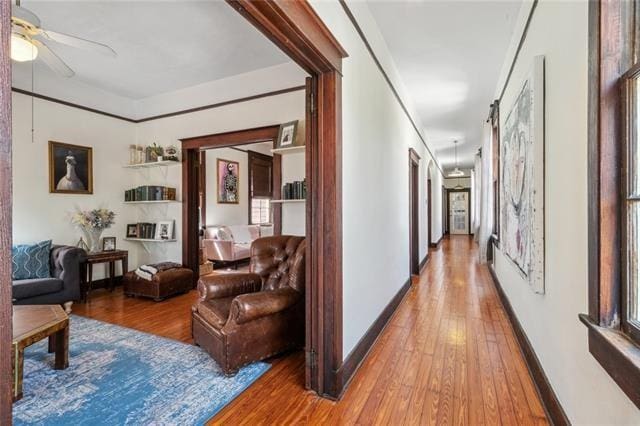 hallway with baseboards, wood finished floors, and ornamental molding