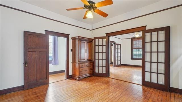 spare room with baseboards, light wood-style floors, ceiling fan, and french doors