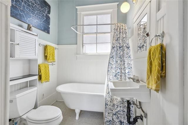 bathroom with a soaking tub, a wainscoted wall, toilet, and tile patterned floors