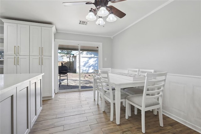 dining space with ornamental molding, light wood finished floors, ceiling fan, visible vents, and wainscoting