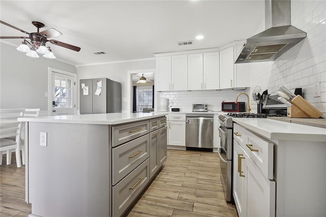 kitchen featuring wall chimney range hood, stainless steel appliances, ceiling fan, and visible vents