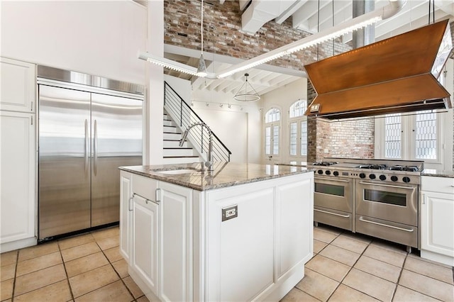 515 Ursulines Ave, New Orleans, LA 70116 - kitchen with premium appliances, premium range hood, a center island with sink, light tile patterned floors, and white cabinets