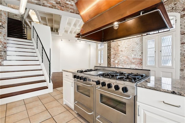 515 Ursulines Ave, New Orleans, LA 70116 - kitchen featuring ventilation hood, double oven range, brick wall, light tile patterned flooring, and white cabinets