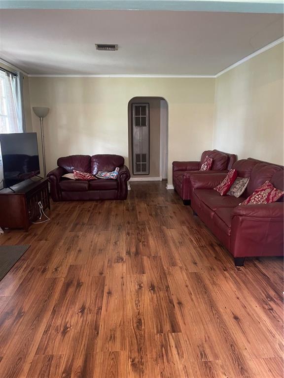 living area with arched walkways, visible vents, crown molding, and wood finished floors