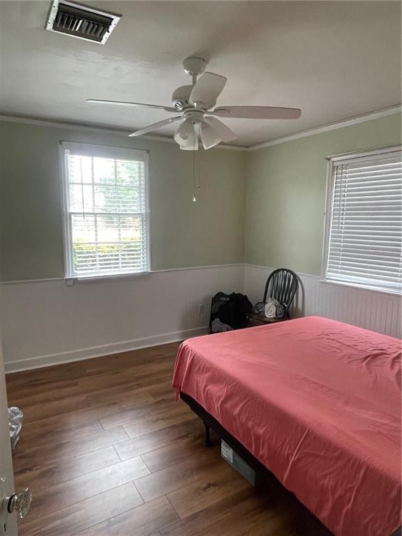 bedroom with ornamental molding, a ceiling fan, a wainscoted wall, visible vents, and wood finished floors