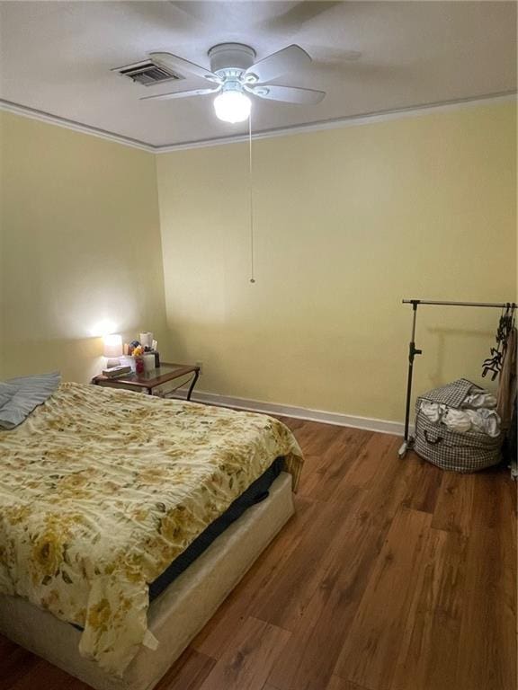 bedroom with ceiling fan, ornamental molding, visible vents, wood finished floors, and baseboards