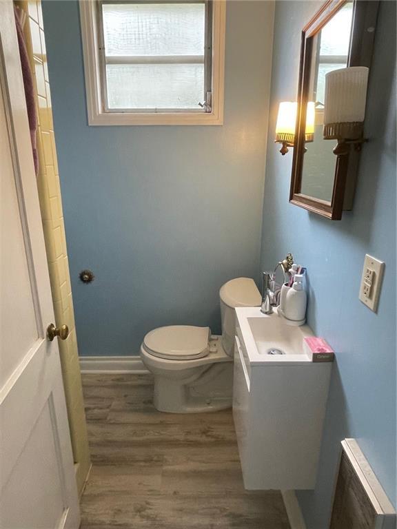half bathroom featuring radiator heating unit, vanity, toilet, wood finished floors, and baseboards