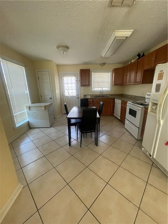 4941 Viola St, New Orleans, LA 70126 - kitchen with white appliances, a textured ceiling, light tile patterned flooring, and brown cabinetry