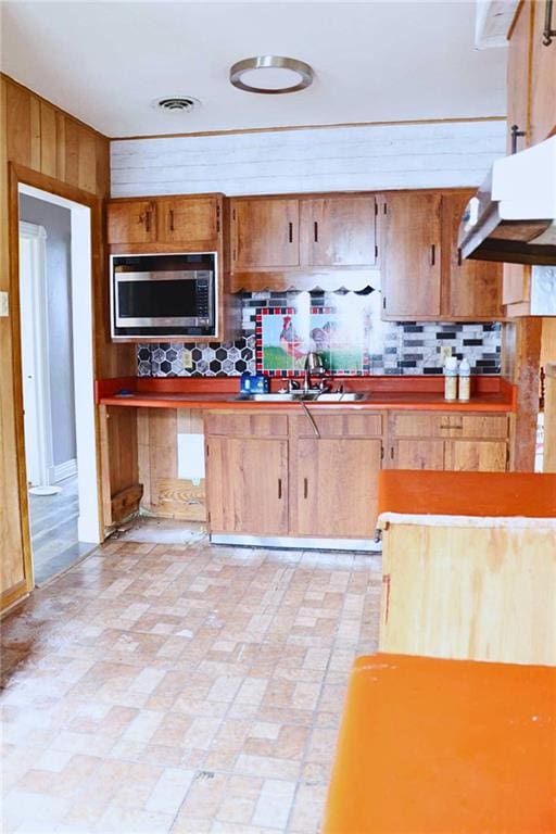 kitchen featuring decorative backsplash, visible vents, wooden walls, stainless steel microwave, and a sink