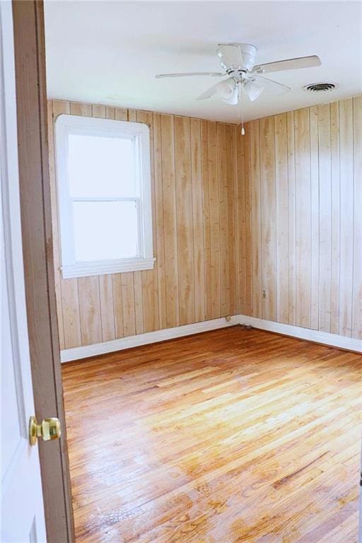 empty room with wood finished floors, wood walls, baseboards, visible vents, and ceiling fan