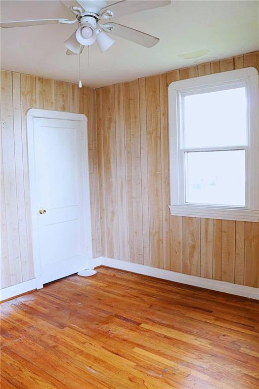 empty room with wood walls, baseboards, ceiling fan, and wood finished floors