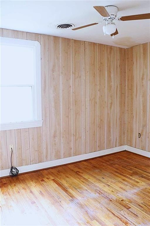 spare room with wood finished floors, wood walls, ceiling fan, and visible vents
