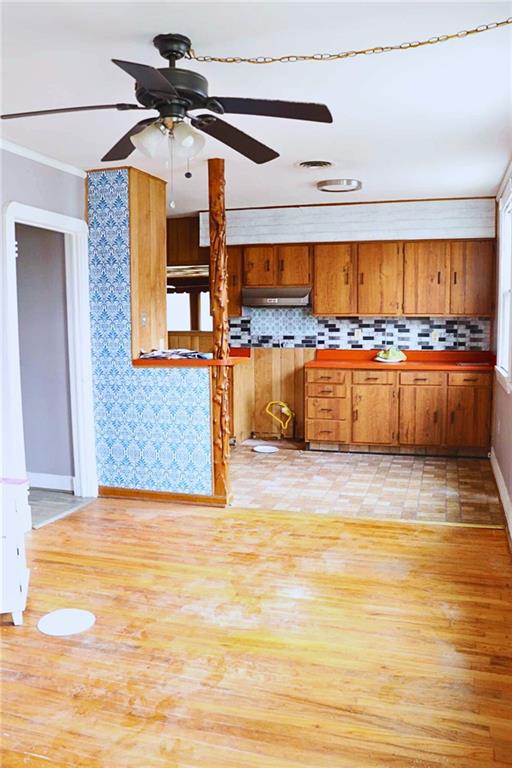 kitchen featuring tasteful backsplash, brown cabinetry, under cabinet range hood, light wood-style floors, and ceiling fan