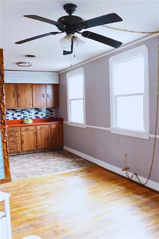 kitchen featuring crown molding, tasteful backsplash, brown cabinetry, baseboards, and ceiling fan
