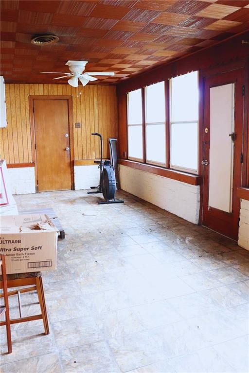 unfurnished living room featuring a ceiling fan, wood walls, and tile patterned floors